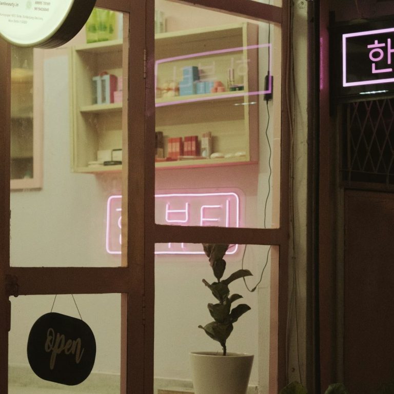 Entrada de una tienda con letreros en neón y una planta decorativa en la ventana.